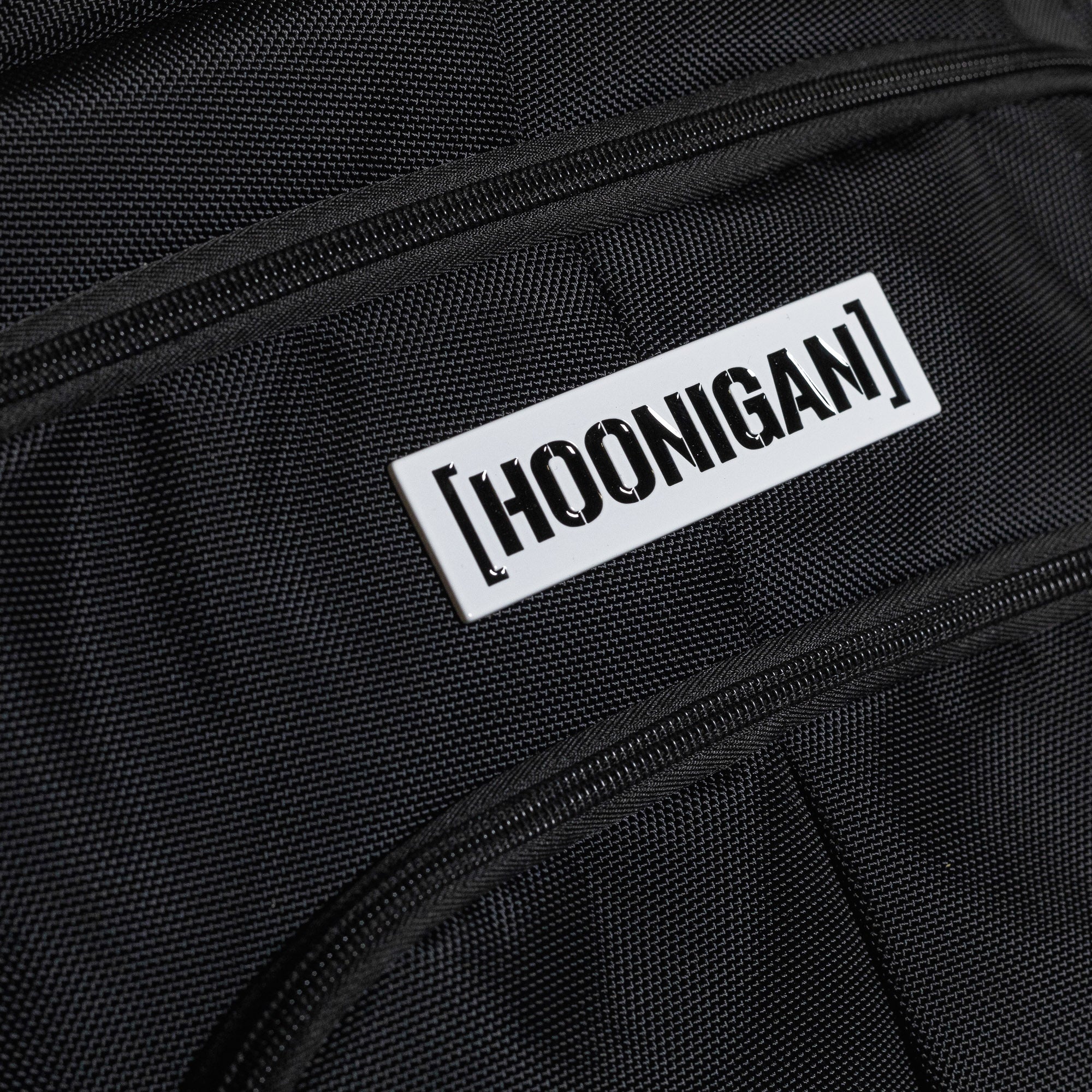 Hoonigan METAL BAR Backpack featuring a rugged black design, adjustable straps, and a prominent logo on the front.