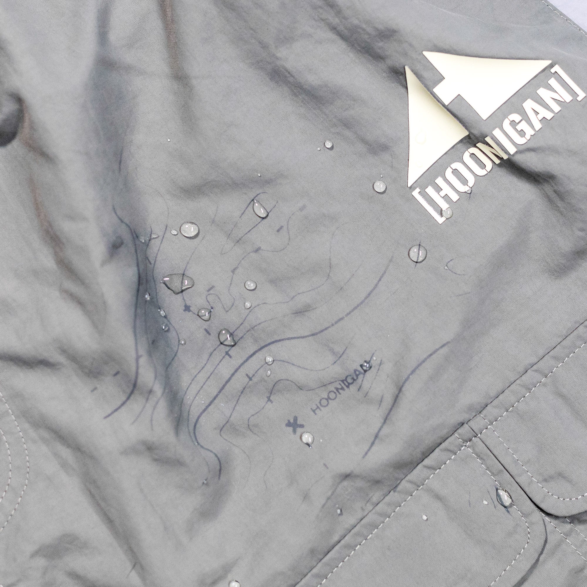Gray Hoonigan H.A.V.O.C. rain-activated cargo shorts with water droplets, logo, and topographic map design.