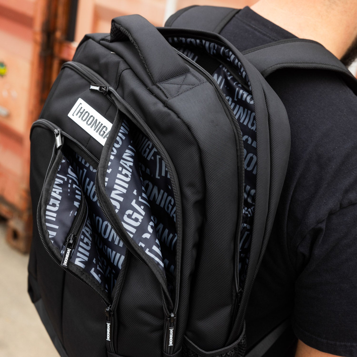 Hoonigan METAL BAR Backpack featuring a black design with bold white logo and adjustable straps.