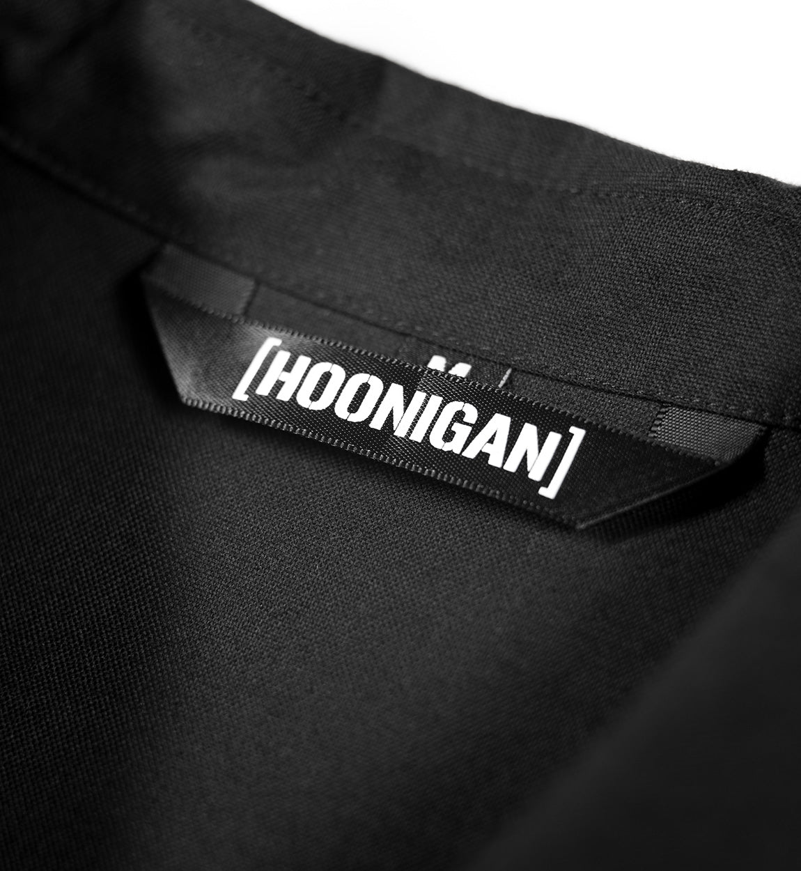 Hoonigan DONUT GARAGE Black Woven Long Sleeve Button-up Shirt displayed on a flat surface, featuring a classic collar and logo detail on the chest.