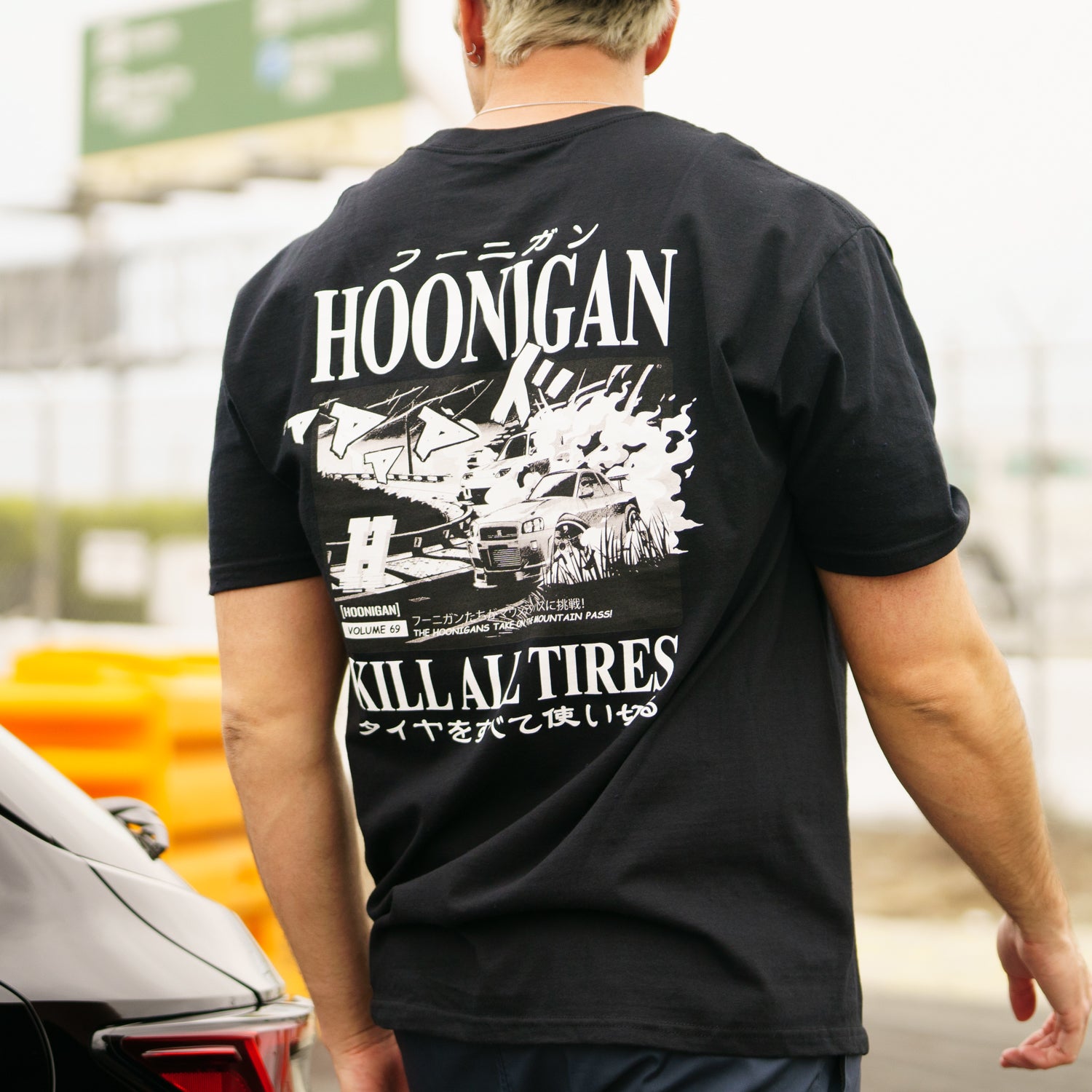 Back view of a person wearing a black Hoonigan Tokyo Drip short sleeve T-shirt with graphic design and Japanese text.